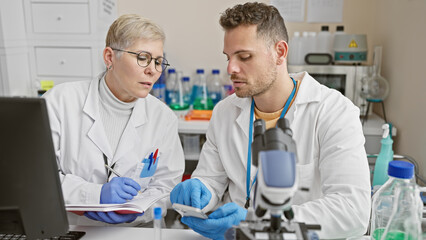 A woman and a man in lab coats work collaboratively in a scientific laboratory, researching with...