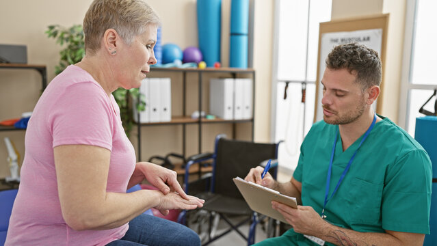A woman consults with a male physiotherapist in a well-equipped rehabilitation clinic room, indicating a professional healthcare scenario.