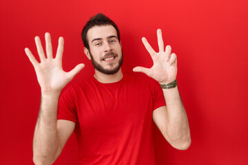 Young hispanic man wearing casual red t shirt showing and pointing up with fingers number eight while smiling confident and happy.