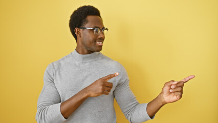 Smiling african american man in casual clothing pointing to side on yellow background.