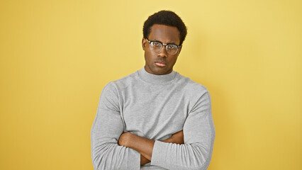Confident adult man with arms crossed wearing glasses against a yellow wall