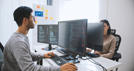 Young adult Asian male, female software developer coding program on desktop computer. Man, woman...