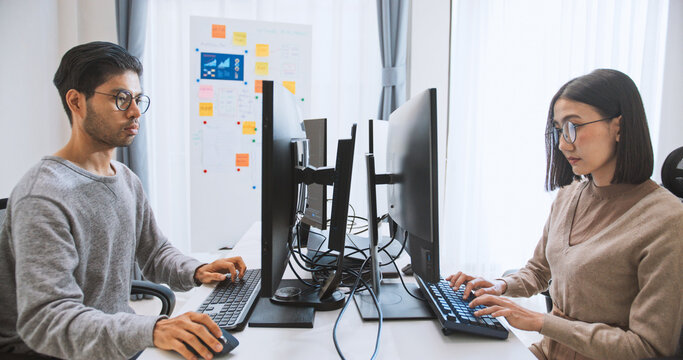 Young adult Asian male, female software developer coding program on desktop computer. Man, woman work from home, remote working, freelance programmer job, smart digital nomad lifestyle concept