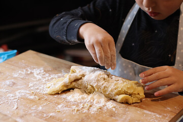 Kid making fancy biscuits halloween cookie cutter pastry dough on the messy wood board. Portrait...