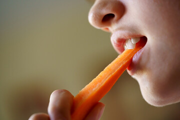 Crop anonymous teenage girl eating fresh organic carrot slice - obrazy, fototapety, plakaty
