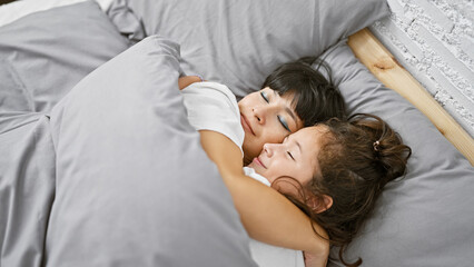 Lying together in their cozy room, a mother and daughter share a loving hug before drifting off to...