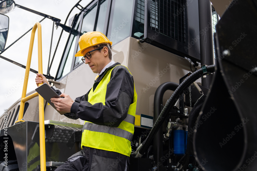 Poster Engineer with tablet computer stands on the stairs to the cab of a truck..