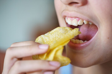 Unrecognizable teenage girl eating crunchy potato chips at home