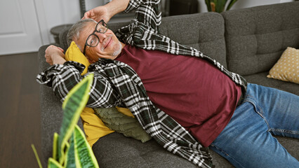 Fototapeta na wymiar A cheerful grey-haired man relaxing on a sofa in a cozy living room, exuding comfort and joy.
