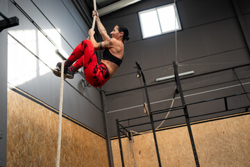 Fit mature woman climbing a rope in a gym