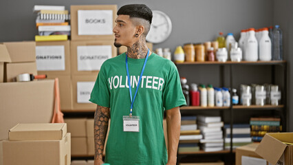 Serious-faced young latin man volunteering at local charity center, his tattooed arms at work...