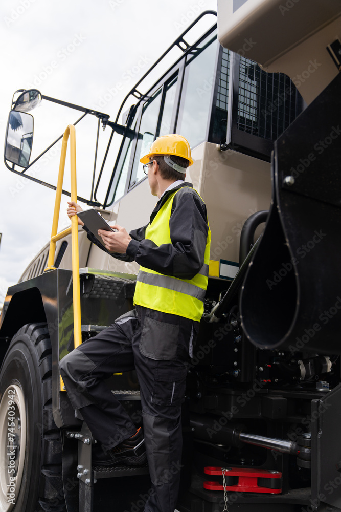 Poster Engineer with tablet computer stands on the stairs to the cab of a truck..