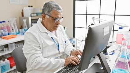 Mature man in lab coat analyzing data on computer in a bright laboratory setting.