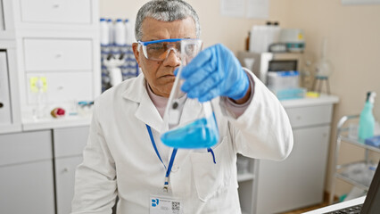 Middle-aged man in lab coat examines contents of a beaker in a laboratory setting, with clinical equipment visible.