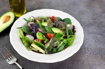 Fresh mix salad with avocado, tomato and radish on a brown background. Avocado salad. 