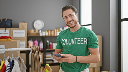 Young hispanic man volunteer smiling confident using smartphone at charity center