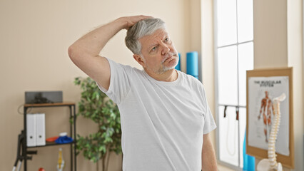 Middle-aged man stretching neck in a physiotherapy clinic interior.