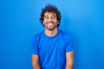 Fototapeta na wymiar Hispanic young man standing over blue background with a happy and cool smile on face. lucky person.