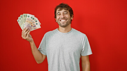 Young, smiling man confidently holding and counting his wealth in argentine pesos banknotes,...