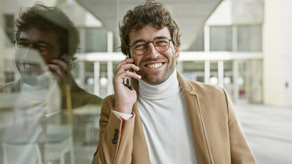 Smiling young hispanic man with beard talking on phone in urban city environment.