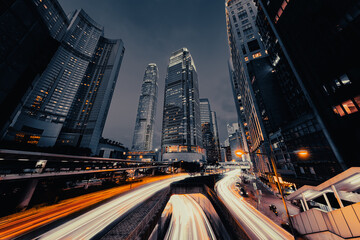 Rush hour in Hong Kong, China with light trails from cars in the foreground an skyscraper in the...