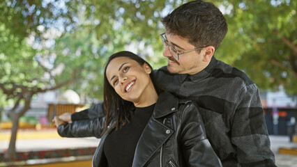 A smiling woman and man embracing each other with affection on a tree-lined urban street.