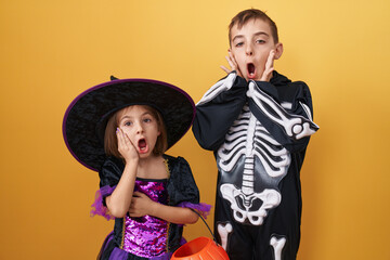 Amazed brother and sister in halloween costumes, mouth open in disbelief, scared yet excited faces against a yellow isolated background. surprised family bonds during a spooky party!
