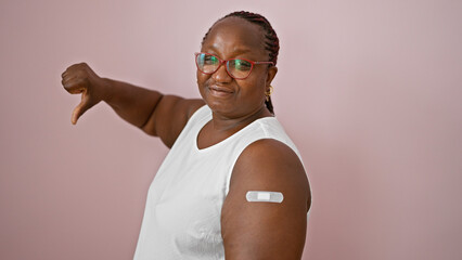 African american woman with arm band aid flashes thumb down sign over serene pink background