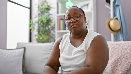 African american woman sitting on sofa with serious expression at home
