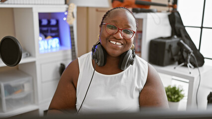 Confident african american woman musician, radiating joy, wearing headphones in a music studio