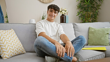Cheerful young hispanic teenager radiates confidence while relaxing and smiling on a cozy sofa, enjoying the comfort of home.