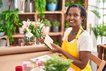 Middle age african american woman florist holding bouquet of flowers and envelope letter at flower shop