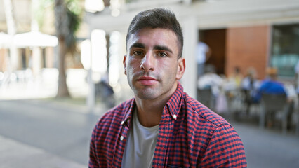 Young hispanic man sitting on bench with serious expression at street