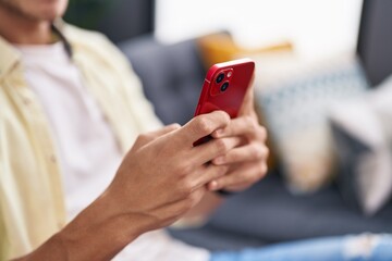 Young hispanic man using smartphone sitting on sofa at home