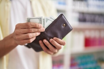 Young hispanic man customer holding dollars of wallet at pharmacy