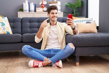 Young hispanic man doing video call with smartphone smiling happy pointing with hand and finger