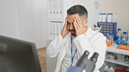 Stressed hispanic man in lab coat feeling headache at medical center.