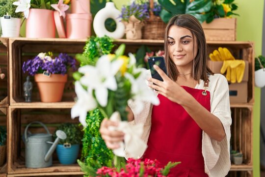 Young beautiful hispanic woman florist make photo to flowers by smartphone at flower shop