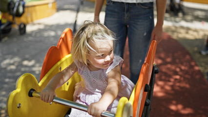 Caucasian mother and willing daughter sitting on a seesaw, playing seriously in the park playground...