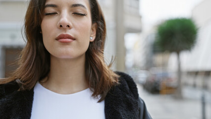 Close-up of a serene hispanic woman with eyes closed in an urban street setting, evoking...