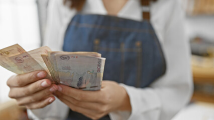 Hispanic woman holding colombian currency inside an indoor setting.