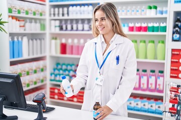 Young blonde woman pharmacist smiling confident holding medication bottles at pharmacy