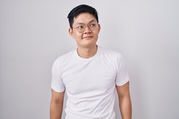 Young asian man standing over white background smiling looking to the side and staring away thinking.