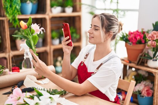 Young blonde woman florist make photo to flower by smartphone at flower shop