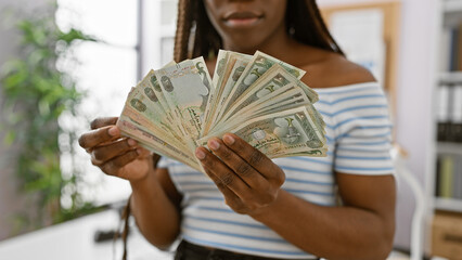 African woman holding dirhams indoors, portraying finance in an office setting with clarity and...