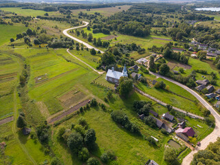 Top view of a small village in the middle of a green field and forest. An old church on a hill in the center of the city. Aerial view of the farm field and the natural landscape.