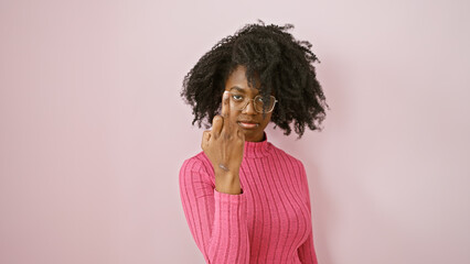 African american woman with glasses in pink sweater posing indoors with neutral background