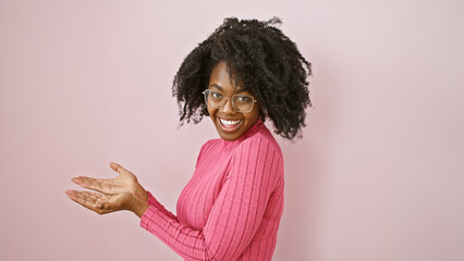 African american woman smiling indoors with glasses and pink sweater gesturing on a plain background.