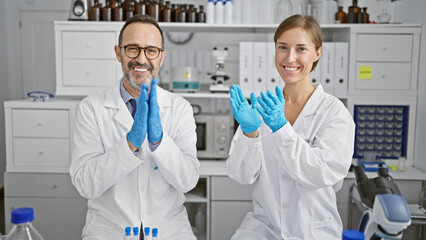 Two smiling scientists clapping hands in applause, celebrating major research breakthrough in their...