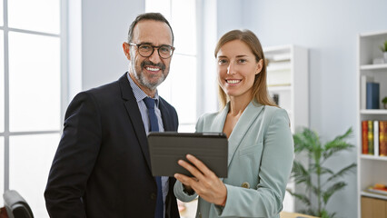 Two confident business workers standing together, enjoying their work at the office, using touchpad...